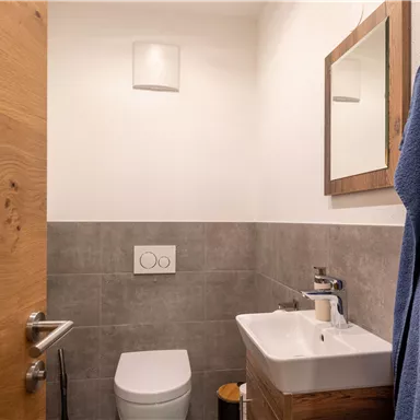 A small, modern bathroom with a white toilet and a sink. A towel is hanging on the wall and a mirror is mounted above the sink.