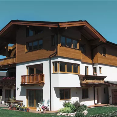 Ein modernes Haus mit Holz- und Putzfassade in den Bergen. Der großzügige Balkon und die Fenster schaffen eine helle, einladende Atmosphäre.