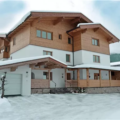 Ein modernes Holzhaus im Schnee, umgeben von einer winterlichen Landschaft. Der Himmel ist bewölkt und die Architektur ist gemütlich und einladend.