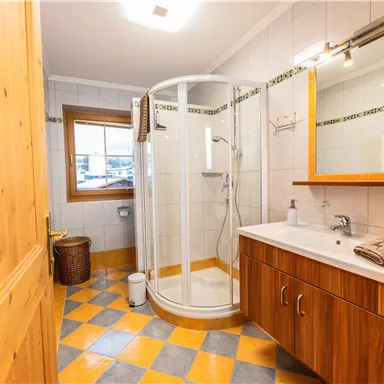 Ein modernes Badezimmer mit einer Dusche und Holzdetails. Der Boden ist mit bunten Fliesen in Gelb und Grau gestaltet.