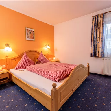 Ein gemütliches Schlafzimmer mit einem Holzbett und lila Kissen. Die Wände sind orange und das Zimmer hat einen Teppich mit einem blauen Muster.