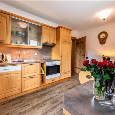 Eine einladende Küche aus Holz mit modernen Geräten. Auf dem Tisch stehen frische Rosen und Gläser, die eine gemütliche Atmosphäre schaffen.