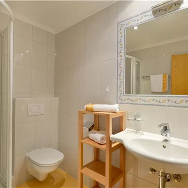 A modern bathroom with a shower, sink, and mirror. Towels and a shelf are visible.