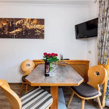 Eine gemütliche Essbereich mit einem Holztisch und Stühlen. Auf dem Tisch steht eine Vase mit roten Rosen und im Hintergrund ein Fernseher.