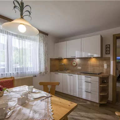 A bright, modern kitchen with white cabinets and a dining table. The window lets in plenty of daylight and offers a view outside.