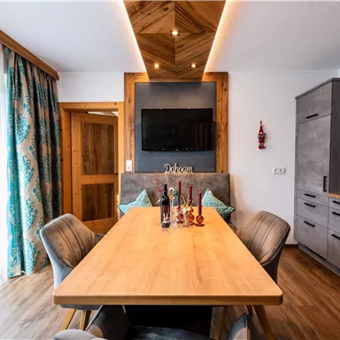 Ein stilvolles Esszimmer mit einem großen Holztisch und modernen Stühlen. Die Fenster sind mit Vorhängen geschmückt, und eine gemütliche Atmosphäre wird durch die warme Beleuchtung erzeugt.