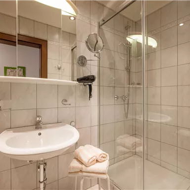 Ein modernes Badezimmer mit einer Dusche und Fliesenwänden. Auf dem Waschbecken liegen frische Handtücher.