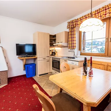 Eine gemütliche Küche mit einem Essbereich aus Holz. Fenster lassen viel Licht hereinfällt und der Raum hat ein einladendes Ambiente.