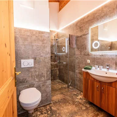 Ein modernes Badezimmer mit einer gläsernen Dusche und einem stilvollen Waschbecken. Die Holz- und Steinakzente schaffen eine warme Atmosphäre.