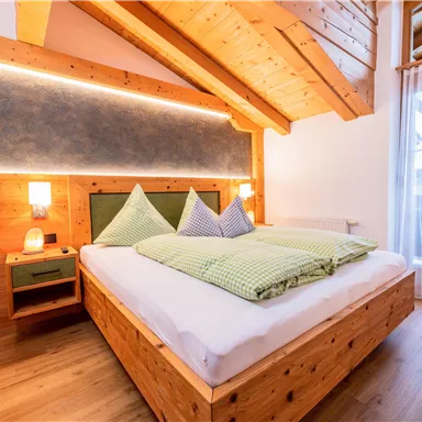 Ein modernes Schlafzimmer mit Holzdekor und einem großen Bett. Der Raum hat große Fenster, die viel Licht hereinlassen.