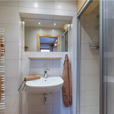 A modern bathroom with a sink, a towel, and a shower. The walls are brightly tiled and there is a large mirror.