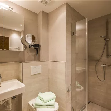 Ein modernes Badezimmer mit hellem Fliesendesign. Es gibt eine Dusche, ein Waschbecken und frische Handtücher.