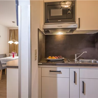 Eine moderne Küche mit Geschirrspüler und Mikrowelle. Im Hintergrund ist ein Essbereich mit einem Tisch und Stühlen sichtbar.