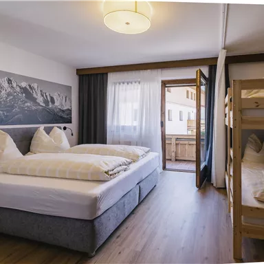 Ein modernes Schlafzimmer mit einem Doppelbett und einem Etagenbett. Große Fenster bieten Blick auf den Balkon und die Umgebung.