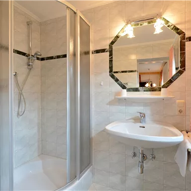 A modern bathroom with a shower and a sink. The walls are light tiled, and there is a large mirror.