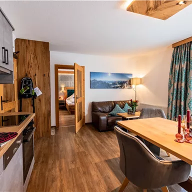 Eine moderne Küche mit Holzdetails und einem gemütlichen Essbereich. Im Hintergrund befindet sich ein Wohnzimmer mit bequemen Möbeln und natürlichem Licht.