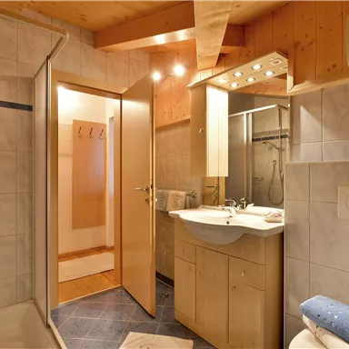 Ein modernes Badezimmer mit Dusche, Waschbecken und Holzverkleidung. Der Raum ist gut beleuchtet und bietet viel Stauraum.