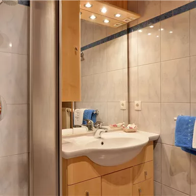 Ein modernes Badezimmer mit hellem Fliesenboden und einem Waschbecken. Neben dem Waschbecken sind Handtücher in Blau und Weiß aufgehängt.