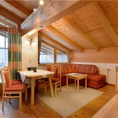 Ein gemütliches Wohnzimmer mit Holzwänden und einem schönen Dach. Es gibt ein Esszimmer, eine Sitzecke und einen kleinen Küchenbereich.