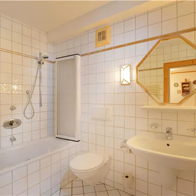 A bright bathroom with white tiles and a bathtub-shower area. There is a sink and a mirror on the wall.