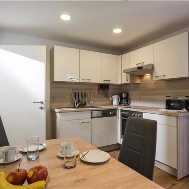A modern kitchen unit with bright cabinets and a dining area. Fresh fruit and dishes are on the table.