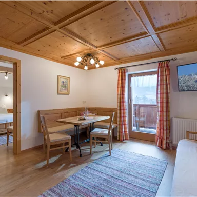 A cozy living space with a wooden ceiling and table. Large windows provide plenty of daylight and offer a view of the balcony.