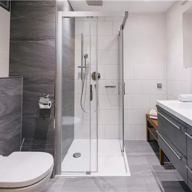 Ein modernes Badezimmer mit einer Dusche und einem Waschbecken. Die Wände sind in hellen und dunklen Farben gehalten, und es gibt einen großen Spiegel.