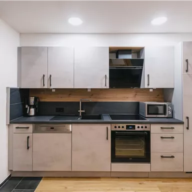 Eine moderne Küche mit grauen Schränken und einem schwarzen Arbeitsplatte. Sie enthält einen Herd, eine Spüle und eine Mikrowelle.