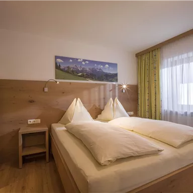 Ein gemütliches Schlafzimmer mit einem Doppelbett und Holzverkleidungen. Das Zimmer hat große Fenster mit Vorhängen und eine harmonische Dekoration.