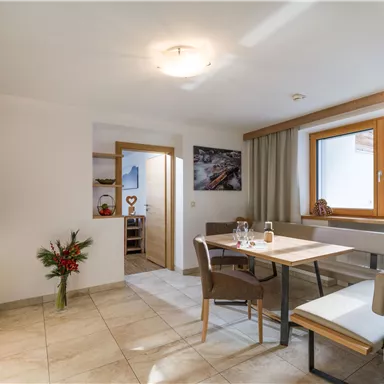 Eine moderne Küche mit einem Esstisch und Stühlen. Ein Fenster lässt viel Licht herein und es gibt dekorative Elemente wie Blumen.