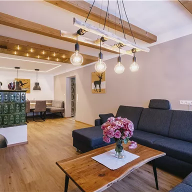 Ein modernes Wohnzimmer mit einem gemütlichen Sofa und einem Holztisch. Die gemütliche Atmosphäre wird durch die dekorativen Lichter und die Holzdetails verstärkt.