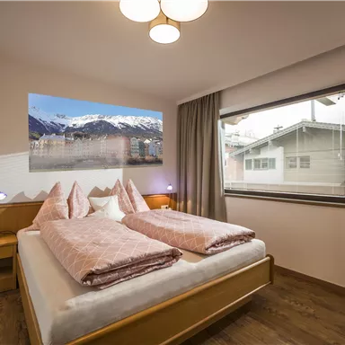 Ein gemütliches Schlafzimmer mit einem Doppelbett und sanften rosa Bettwäsche. Große Fenster bieten einen Blick auf die Berge und das Tageslicht strömt herein.