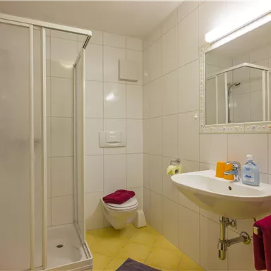 Ein modernes Badezimmer mit Dusche, Waschbecken und Spiegel. Rote Handtücher und Pflegeprodukte sind vorhanden.