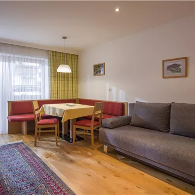 Ein gemütliches Wohnzimmer mit einem grauen Sofa und einem Essbereich. Große Fenster lassen viel Licht herein und bieten einen Blick nach draußen.