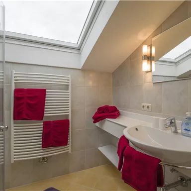 Ein modernes Badezimmer mit einem großen Fenster und eleganten Armaturen. Rote Handtücher verleihen dem Raum einen frischen Akzent.