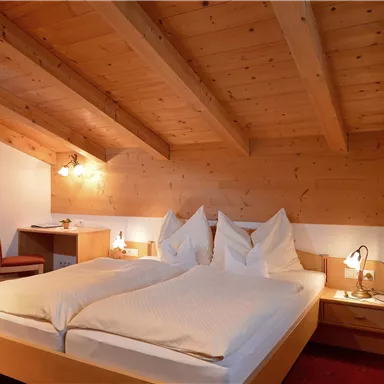 Ein gemütliches Schlafzimmer mit einem Doppelbett und Holzdecken. Es gibt einen Schreibtisch und warme, einladende Farben.