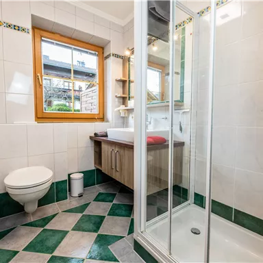 Ein modernes Badezimmer mit Dusche und Waschbecken. Der Boden ist in einem ansprechenden Muster aus grünen und weißen Fliesen gestaltet.