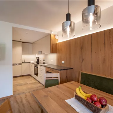 Modern kitchen with wooden details and a dining table. On the table, there is fruit and a small television is mounted on the wall.