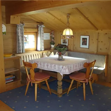 Ein gemütlicher Essbereich in einem Holzhaus mit einem runden Tisch und Stühlen. Die Wände sind aus Holz, und es gibt Vorhänge und eine warme Beleuchtung.