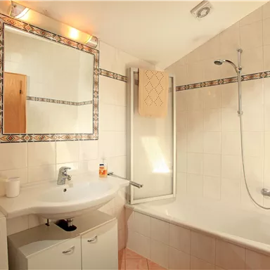 Ein modernes Badezimmer mit einer Badewanne und einer Dusche. Der Raum ist gut beleuchtet und hat helle Fliesen.