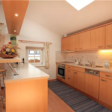 Eine moderne Küche mit Holzschränken und Edelstahlgeräten. Der Raum ist hell und einladend, mit einem Essbereich und einer gemütlichen Atmosphäre.