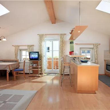 Eine moderne, helle Wohnküche mit Holzfußboden und hohen Decken. Es gibt einen Essbereich, eine voll ausgestattete Küche und große Fenster für viel Tageslicht.