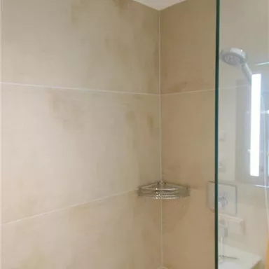 Eine moderne Dusche mit beige Fliesen und einer Glaswand. Der Regenduschkopf ist an der Decke montiert.