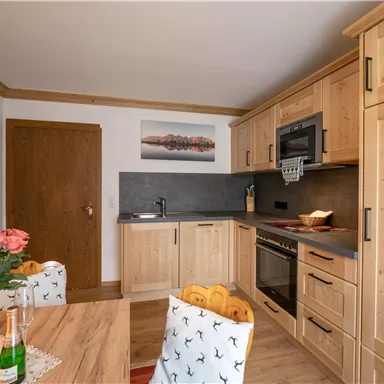 Eine moderne Küche mit Holzschränken und einer eleganten Arbeitsplatte. Am Tisch stehen frische Blumen und Getränke bereit.