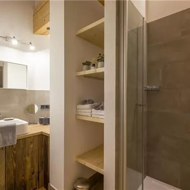 Ein modernes Badezimmer mit einer Dusche, einem Waschbecken und Holzregalen. Die Wände sind in neutralen Farbtönen gehalten, und es gibt dekorative Pflanzen.