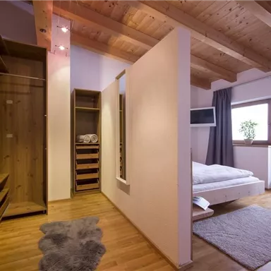 Ein modernes Zimmer mit Holzdecke und einem gemütlichen Bett. Es gibt einen Kleiderschrank und Zugang zu einem Balkon mit Aussicht.