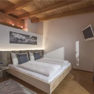 Ein modernes Schlafzimmer mit einem Doppelbett und Holzboden. Große Fenster und eine gemütliche Atmosphäre sorgen für einladendes Wohnen.