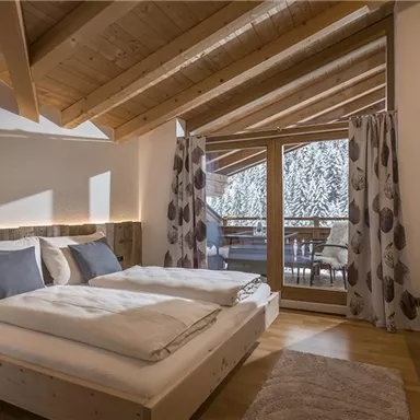 Ein modernes Schlafzimmer mit zwei Einzelbetten und gemütlicher Dekoration. Große Fenster bieten Blick auf einen Balkon und Natur.