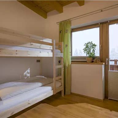 Ein helles Schlafzimmer mit Hochbett und einem großen Fenster. Pflanzen sorgen für eine angenehme Atmosphäre.