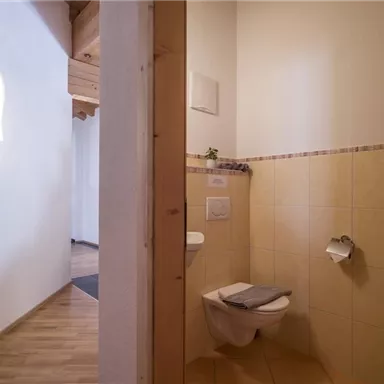 Ein kleines, sauberes Badezimmer mit hellen Fliesen. Links ist ein WC und rechts ein Urinal, daneben ein Handtuch.